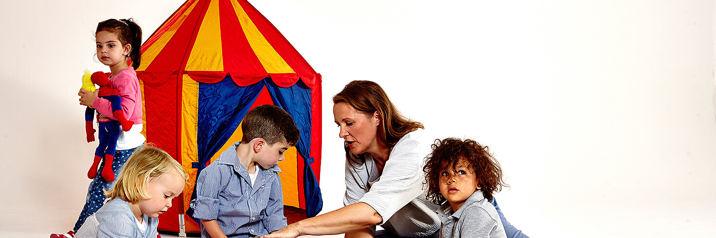 4 kleine Kinder spielen am Boden vor einem Kinderzelt mit der Betreuerin.
