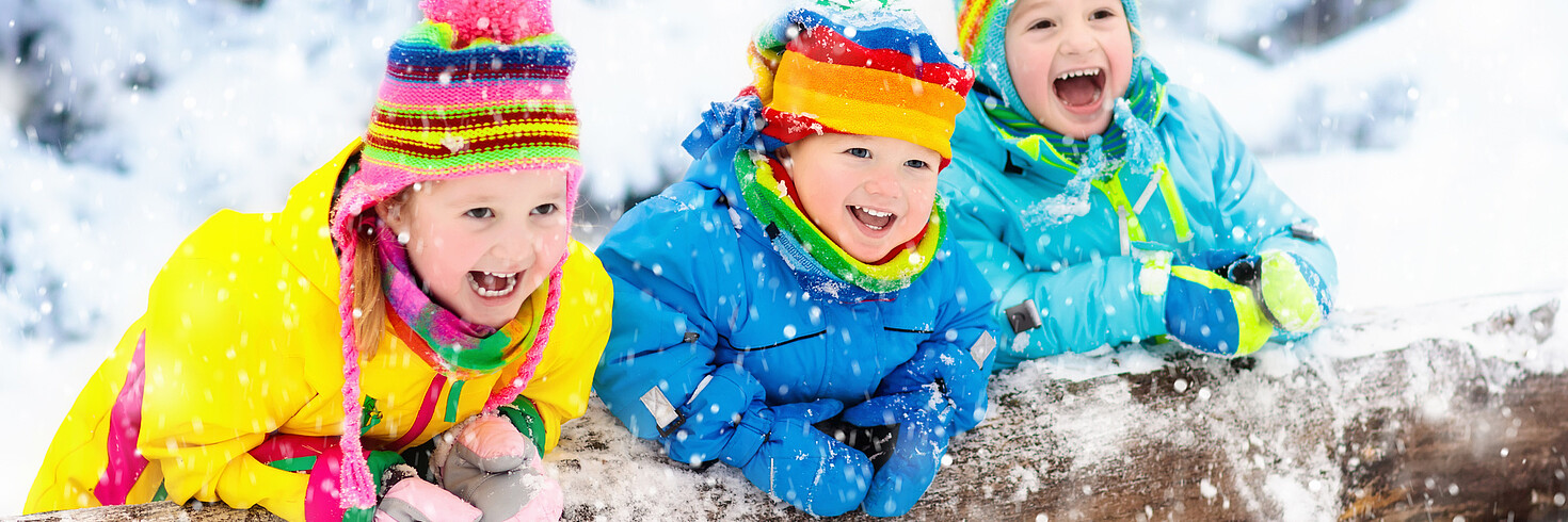 Winter_Drei im Anorak eingepackte Kinder lachen in Kamera