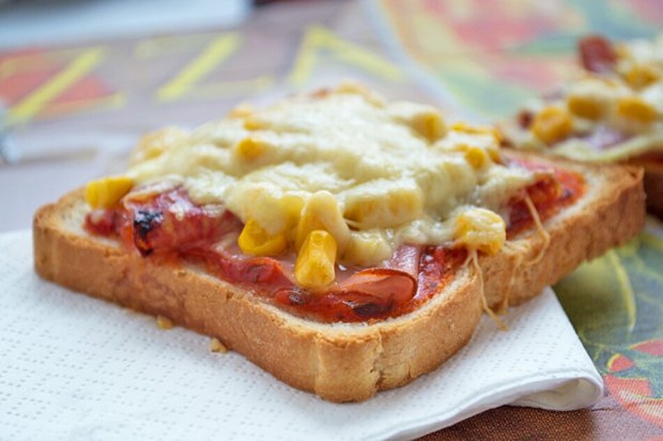 Auf einem Blatt Küchenrolle liegt ein Toast, der mit Tomatensoße und Käse bedeckt ist.